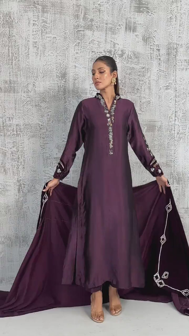 VIDEO: A woman wearing a plum silk long tunic and a dark purple velvet shawl with white embroidery.

